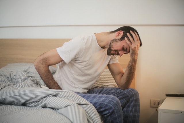 Man die piekert op bed, met zijn hoofd in zijn hand