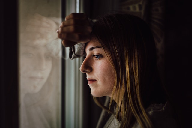 Vrouw die peinzend uit het raam kijkt.