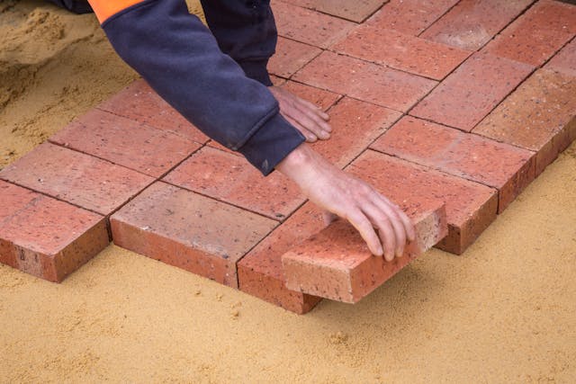 Hand van een stratenmaker die zorgvuldig een steen legt tussen de andere stenen, als symbool voor het langzaam en geduldig opbouwen van vertrouwen.