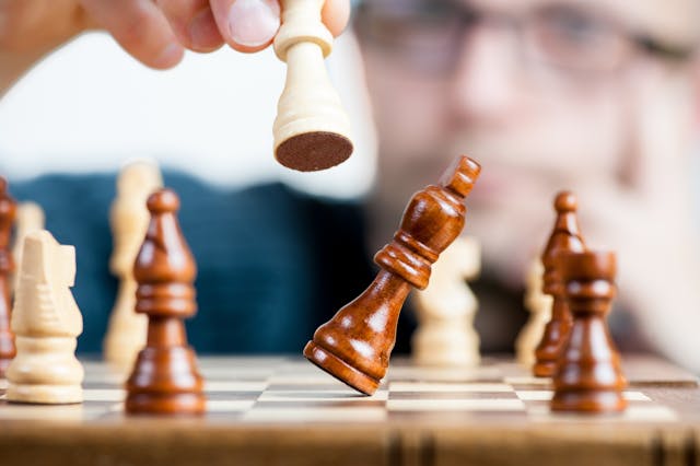 Hand houdt schaakstuk vast en slaat de koning van de ander om — symbool voor controle en machtsstrijd in relaties.