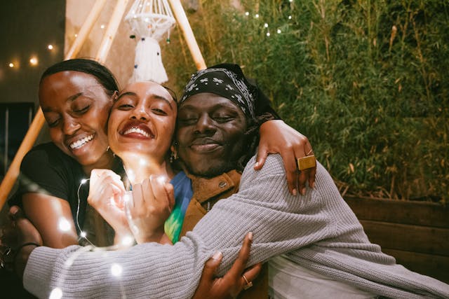Vrouw die liefdevol wordt omarmd door een man en een vrouw, stralend van steun en verbondenheid in een warme familiebijeenkomst.