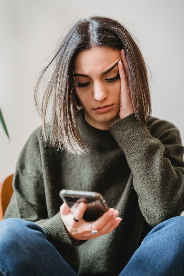 Jonge vrouw staart onzeker naar haar telefoon, blijft stil staan in afwachting van een teken van haar ex.