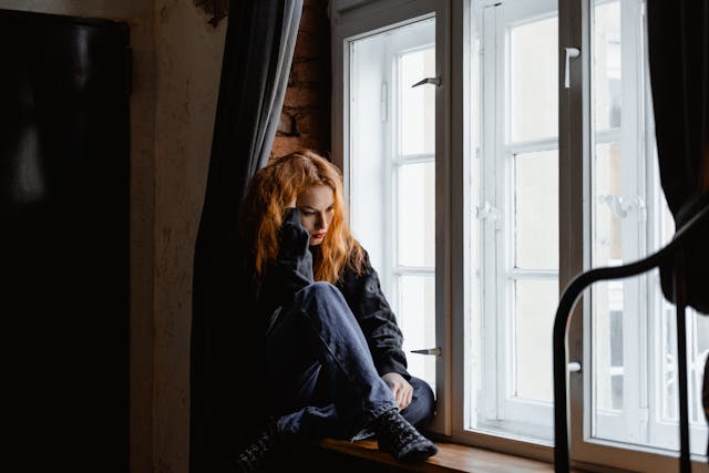 Vrouw zit piekerend op de vensterbank, diep in gedachten over haar beslissing om de relatie te beëindigen.