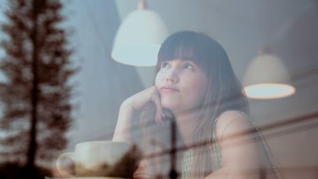 Vrouw die nadenkt en verlangend uit het raam kijkt in een café