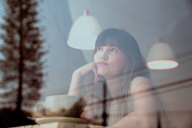 Vrouw die nadenkt en verlangend uit het raam kijkt in een café