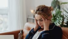 Vrouw zit verslagen op de bank met haar hoofd in haar handen nadat haar man heeft gezegd dat hij wil scheiden; zij wil dit niet en worstelt met het verdriet.
