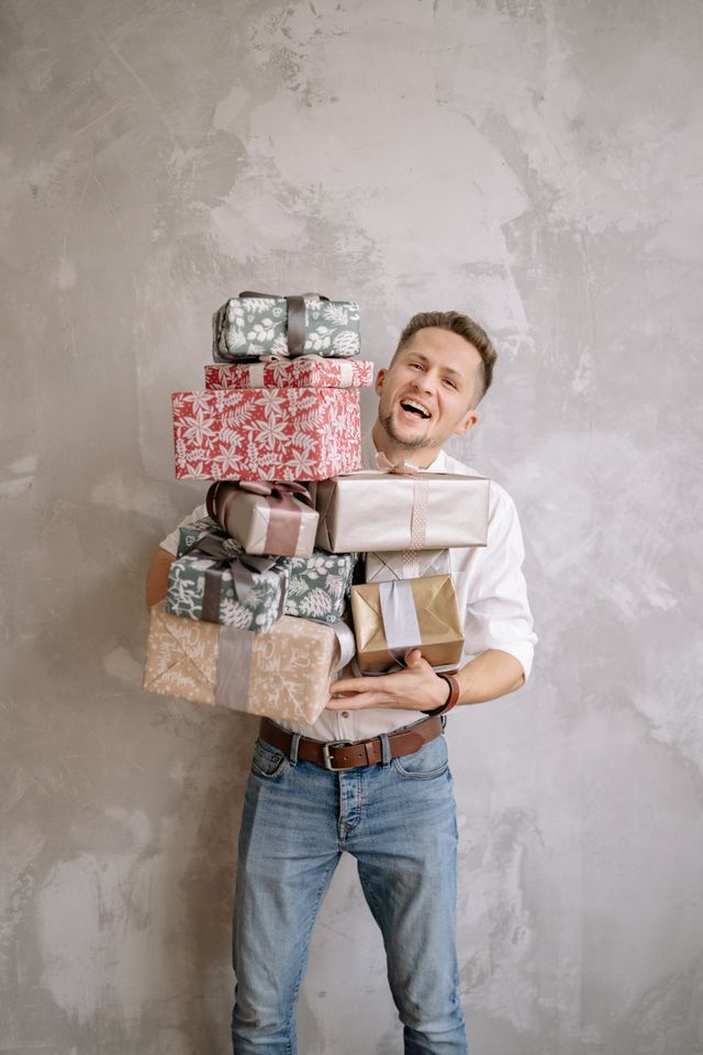 Man lacht sullig met een grote stapel cadeaus, alsof hij alles voor zijn ex over heeft.