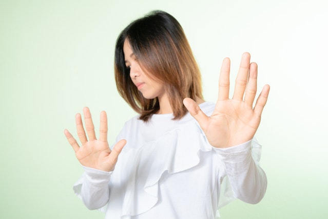 Jonge vrouw maakt met haar handen een afwerend gebaar, symboliseert het bewaken van haar grenzen en zelfrespect.