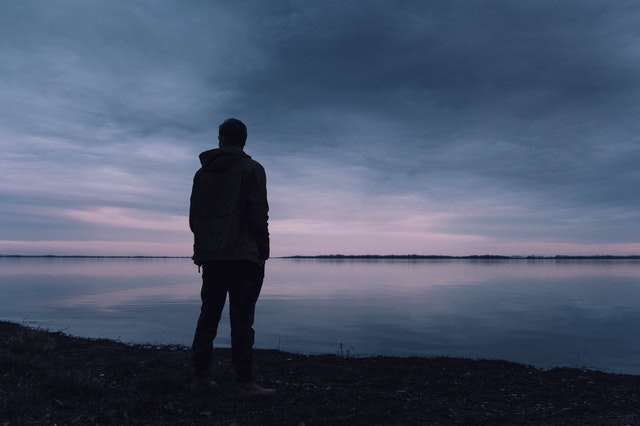 Silhouet van een man die in de avondschemering over het water kijkt.