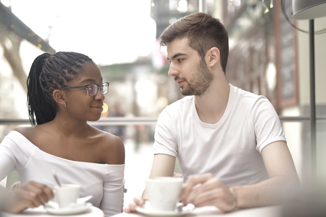 Man en vrouw zitten naast elkaar met een kopje koffie en hebben een eerlijk gesprek over hun verzoening na een gebroken hart.